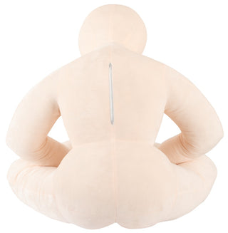 Beige plyschkudde i människoform med dragkedja på baksidan, avbildad sittande med benen i kors.