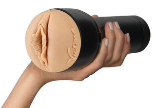 En hand håller Feel Victoria June Masturbator, en köttfärgad vuxenleksak med ett svart fodral och verklighetstrogen texturerad öppning för en autentisk upplevelse.