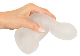 En hand håller i Rebel Penissleeve Med Kulring, en genomskinlig, flexibel silikonhylsa med rundade ändar.