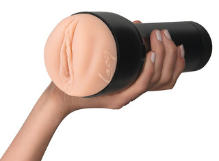 En hand håller i Feel Lacy Lennon Masturbator - en köttfärgad manlig sexleksak med en vulva-liknande öppning, svart fodral och Kiiroo-design för realistisk onani.