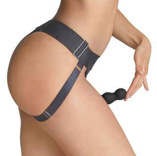 Svart strap-on harness-jock med pärlbandsdetalj, visad från sidan mot en enfärgad bakgrund.