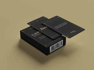 Guilty Pleasure Erotisk Kortlek-kort med guldfärgad text och uppmaningar till parspel, delvis ur en svart låda, visas på en beige yta.