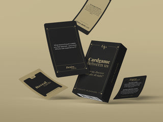 Snygg svart och guldfärgad ask för Guilty Pleasure Erotisk Kortlek, med flera kort som flyter på en beige bakgrund - perfekt som ett spännande kortspel för par.