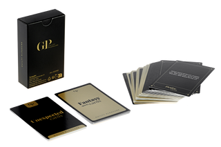 Spelet Guilty Pleasure Erotisk Kortlek, som har en elegant design i svart och guld, visas med sin låda och flera kort utspridda på en vit yta.