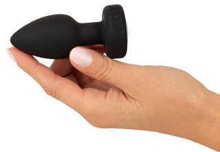 En hand som håller i en svart LED Buttplug med Vibration med LED-belysning mot en vit bakgrund.
