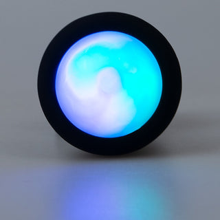 Ett blåvitt virvlande ljus med LED-belysning lyser från LED Buttplug med Vibration, inkapslad i en svart cirkulär ram på en slät yta.