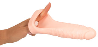 En hand sträcker ut en köttfärgad silikonhylsa, känd som Double Fucker Med Vibration, med en strukturerad exteriör, perfekt för att förstärka känslan när den används med en kulvibrator.