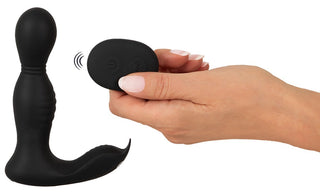 En hand håller en fjärrkontroll bredvid RC Buttplug 2 Funktioner, en elegant, svart silikonvibrator med en böjd design för förbättrad prostatastimulering.