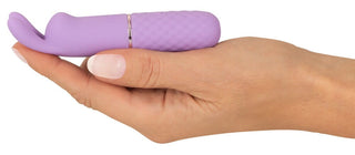 En hand håller Mini Vibrator Cuties Med öron, en liten lila silikonvibrator med en kaninformad ände gjord av silkeslent material.