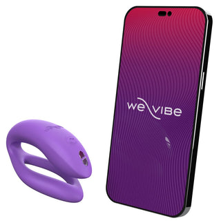 En lila WE-Vibe Sync O Vibrator vilar bredvid en smartphone med en lila och röd gradientskärm med vågiga linjer, som visar "We Vibe", vilket tyder på sömlös integration med We-Vibe-appen.