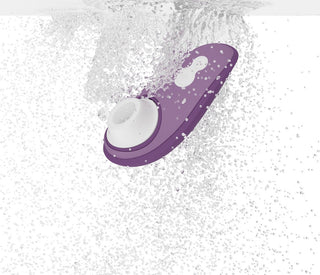 Womanizer Liberty 2 Luftvibrator, en lila och vit handhållen enhet, använder Pleasure Air Technology och kan sänkas ner i vatten och skapa bubblor och stänk.
