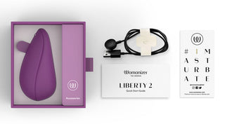 En Womanizer Liberty 2 Luftvibrator med avancerad Pleasure Air-teknik finns i en låda märkt "Tillbehör" tillsammans med en laddningskabel, snabbstartsguide och ett "#IMASTURBATE"-kort med en webbplatslänk. Den idealiska luftvibratorupplevelsen väntar.