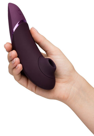 En hand håller Womanizer Next 3D Luftrycksvibrator, med Smart Silence-teknik. Den har en slät utsida, cirkulär öppning, avsmalnande spets och glansig accentring, som liknar en personlig massageapparat eller elektronisk pryl för ökad komfort och lugn.