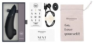 Womanizer Next 3D Luftrycksvibrator i svart kommer i förpackning med Smart Silence-teknologi. Den innehåller en laddningskabel, snabbstartsguide, en väska med texten "Go. Love yourself!" och ett kort med "#IMASTURBATE.