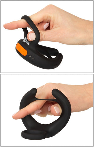 Hand som håller i Vibrerande Scrotumstimulator Rebel, en svart silikon cockring med orange accenter, visad från två vinklar.