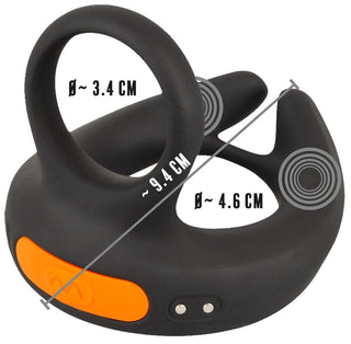 Vibrerande Scrotumstimulator Rebel är en elegant svart och orange elektronisk enhet med två öglor och märkta dimensioner, möjligen designad som en bärbar teknisk komponent.