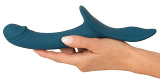 En hand som håller i "Strap-On Set med Vibrator", en ergonomiskt formad, mörkblå silikonenhet för internt bruk, med ett böjt skaft och en utsvängd bas.