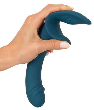 En hand håller Strap-On Set med Vibrator, en blågrön, dubbeländad silikonvibrator med ett böjt handtag och grenad förlängning. Designen är ergonomiskt tilltalande och erbjuder mjuka texturer och konturer för en förbättrad upplevelse.