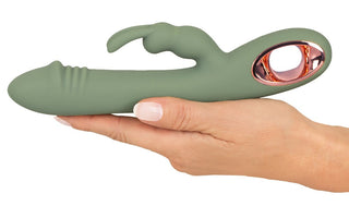 En hand håller Slim Rabbit Vibrator Olive, tillverkad av silkeslen silikon. Den har en grön böjd design med ett guldöglahandtag, som erbjuder dubbla stimulanser via en flexibel klitorisstimulator med dubbla utsprång och räfflade spetsdetaljer.