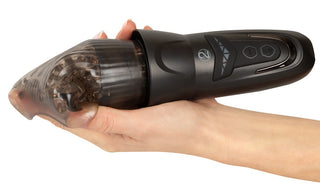 En hand håller en svart Stroker Penis Masturbator med skräp synligt inuti det genomskinliga munstycket.