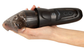 En hand håller en svart Stroker Penis Masturbator med skräp synligt inuti det genomskinliga munstycket.