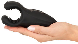 En hand håller Rebel Man Wand Masturbator, en svart silikonanordning med en öppen, texturerad, klämliknande ände utformad för kraftfulla vibrationer.