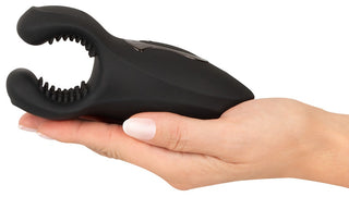 En hand håller Rebel Man Wand Masturbator, en svart silikonanordning med en öppen, texturerad, klämliknande ände utformad för kraftfulla vibrationer.