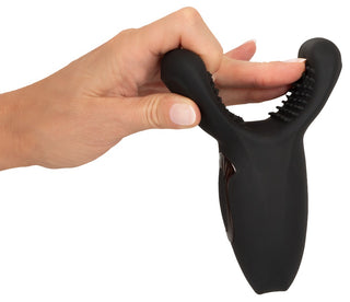 En hand håller Rebel Man Wand Masturbator, en svart silikonanordning med två texturerade stift designade för kraftfull vibration och intensiv penisonani-njutning.