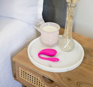 En WeVibe Jive 2 i rosa och ett ljus sitter elegant på nattduksbordet ovanpå en vit rund bricka, perfekt förenar komfort med innovation.
