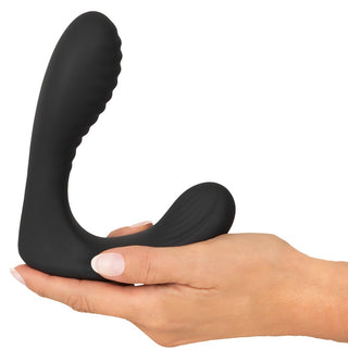 En hand som håller i Intense Prostata Vibrator RC, en svart analvibrator i silikon med en böjd, räfflad design, mot en vit bakgrund.