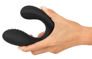 En hand håller Intense Prostata Vibrator RC, en svart, U-formad prostataplugg i silikon med texturerade ytor.