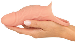 En hand håller en rosa Realistixxx RealSleeve Close, med en strukturerad, detaljerad yta med en handtagsögla för grepp. Denna vibrerande penissleeve liknar en realistisk form.