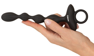 En hand som håller i ANOS flexibla analpärlor i svart, med ett praktiskt ringhandtag.