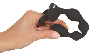 En hand håller i ANOS Flexible Anal Beads, en ringformad vuxenleksak i svart silikon med strukturerade delar.