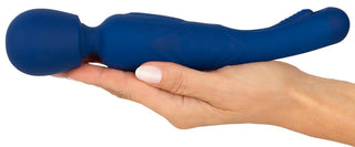 En hand håller en blå "2in1 Wand med Flicking Tongue" massageapparat, med ett runt huvud och böjt handtag med silikonfinish, mot en vit bakgrund.