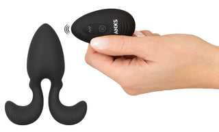 En hand håller en fjärrkontroll bredvid Buttplug med Flexibla Armar - en svart vibrerande analplugg med böjda handtag för kraftfull stimulans och njutningsfull kontroll.