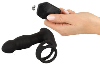 En hand håller i Prostatavibrator Med Fjärrkontroll Rebel, en svart vibrerande dildo med fjärrkontroll och påsatt penisring för ökad njutning och stimulering.