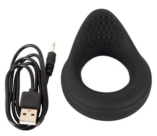 Vibrerande Ballring Rebel, en svart silikonsexleksak med texturerad yta, ligger bredvid en USB-laddningskabel på vit bakgrund.