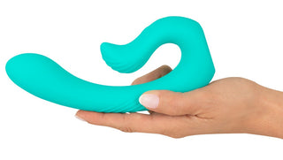 En hand håller NAIRA Dual Heads Vibrator, en flexibel, turkos silikonapparat med 10 vibrationslägen, mot en vit bakgrund.