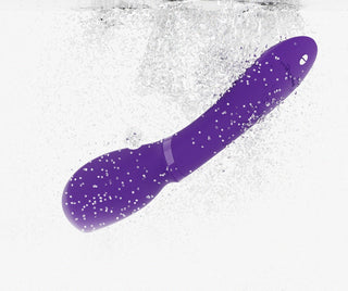 We-Vibe Wand 2, en lila böjd vibrator med Smart Silence-teknik, är under vattnet med luftbubblor runt den mot en vit bakgrund.