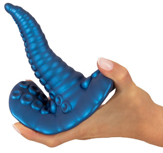 En hand håller Tentacle Pad Sit On Vibrator, en blå, tentakelformad leksak med sugkoppar och en texturerad yta för handsfree-stimulering.
