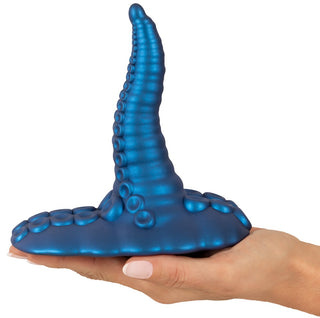 En hand håller Tentacle Pad Sit On Vibrator, en blå silikonvibrator med tentakelform och sugkoppsdetaljer för handsfree-stimulering.