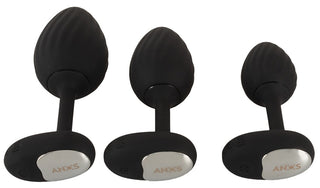 ANOS RC Buttplug Set innehåller tre svarta silikonpluggar med silverfärgade baser i storlekarna small, medium och large. Njut av nya sensationer och enkel kontroll med den medföljande trådlösa fjärrkontrollen för anpassningsbara vibrationer.