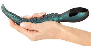 En hand håller i Octo Vibes Tentakel Vibrator i teal, tillverkad av premiumsilikon med verklighetstrogna sugkoppsdetaljer.