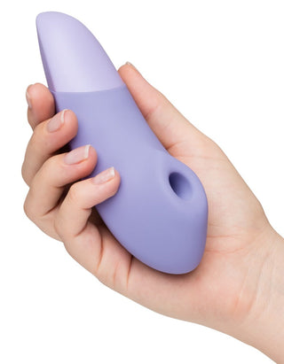 En hand håller en lila, ergonomisk Womanizer Enhance Luftvibrator i silikon, med ett hål nära botten och eventuellt med Pleasure Air Technology, mot en skarp vit bakgrund.