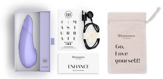 En lila Womanizer Enhance Luftvibrator kommer med en svart USB-laddningskabel, beige ficka med "Go.Love yourself!" text och snabbstartsguide. Njut av Pleasure Air Technology och dela din glädje med #IMASTURBATE.