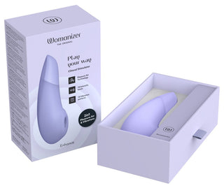 En bild visar den ljuslila Womanizer Enhance Luftvibratorn med dess låda, som framhäver Pleasure Air Technology. "Spela på din väg"-förpackningen öppnar lådan för att avslöja enheten snyggt inuti.