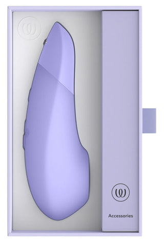 I lådan visas en elegant lila Womanizer Enhance Luftvibrator med ett tillbehörsfack till höger. Dess minimalistiska design har logotyper i båda hörnen och ett ljust färgschema som kompletterar dess innovativa Pleasure Air Technology.