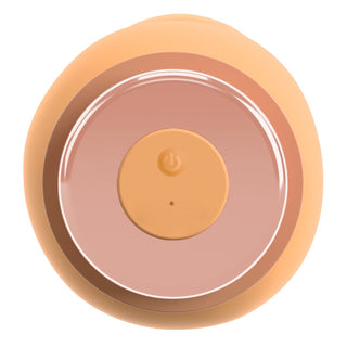 Cirkulär persikofärgad silikonvibrator med central strömknapp och indikatorlampa, sedd uppifrån.