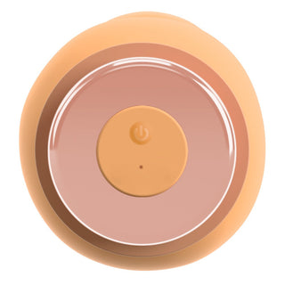 Cirkulär persikofärgad silikonvibrator med central strömknapp och indikatorlampa, sedd uppifrån.